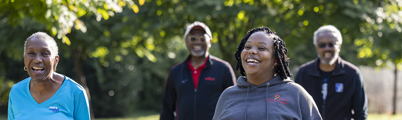 Four people walking and smiling with trees in the background